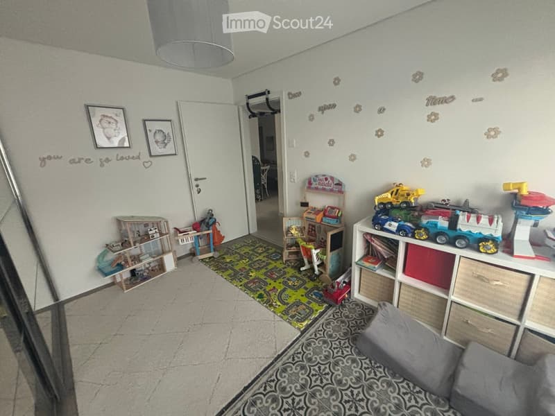 A well-lit children's room with a colorful play area, shelves filled with toys, a small sofa, and decorative wall art.