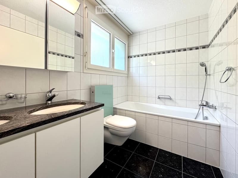 Modern bathroom with white tiles, black floor, sink with faucet, toilet, bathtub, and showerhead.