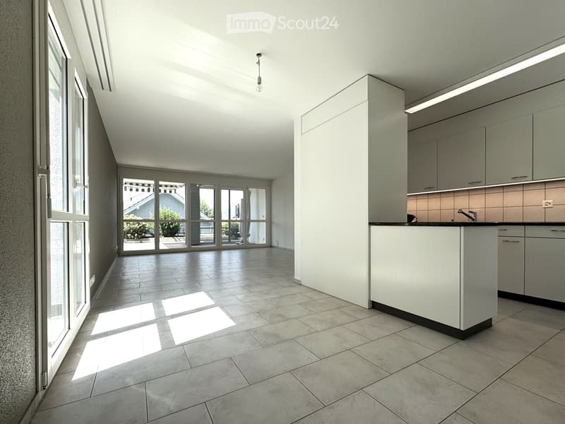 Empty kitchen with modern cabinets, tiled floor, and large windows letting in natural light.