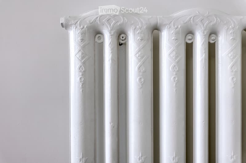 White decorative radiator with ornate patterns and vertical bars mounted on a plain wall.