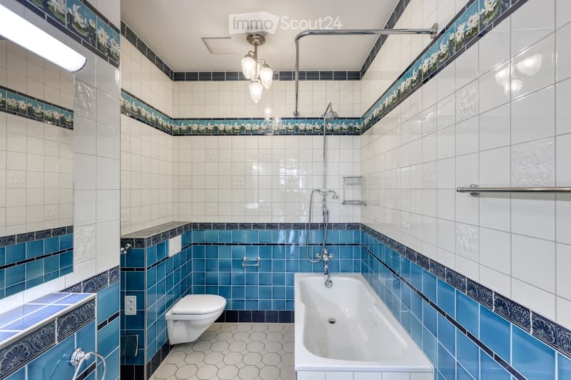 Elegant bathroom with white and blue tiles, floral border design, bathtub, toilet, and modern showerhead.
