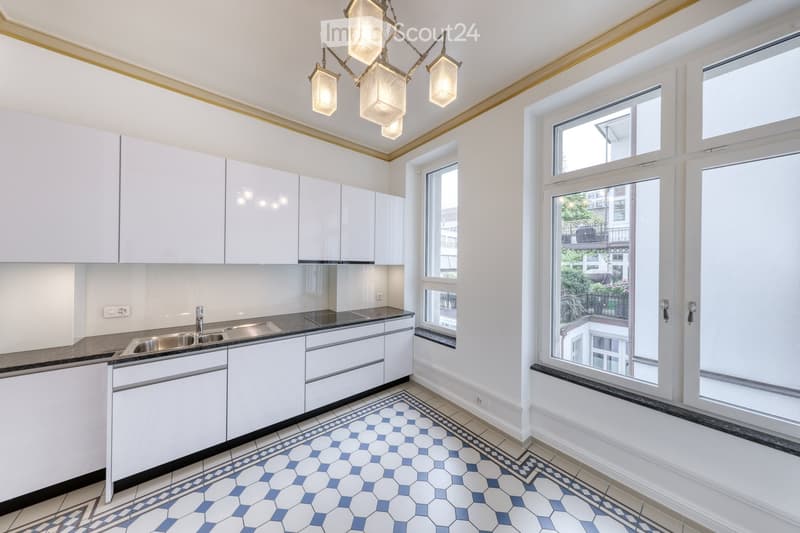 Modern kitchen with white cabinets, stainless steel sink, and a decorative chandelier. The floor features a blue and white hexagonal tile pattern.
