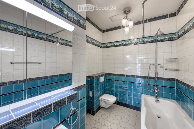 Elegant bathroom with white and blue tiles, floral border design, bathtub, toilet, and showerhead.