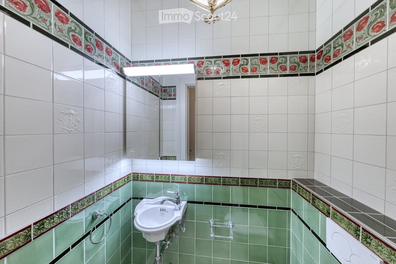 Bathroom with white tiled walls, green tiled floor, decorative floral border, sink, mirror, and toilet.