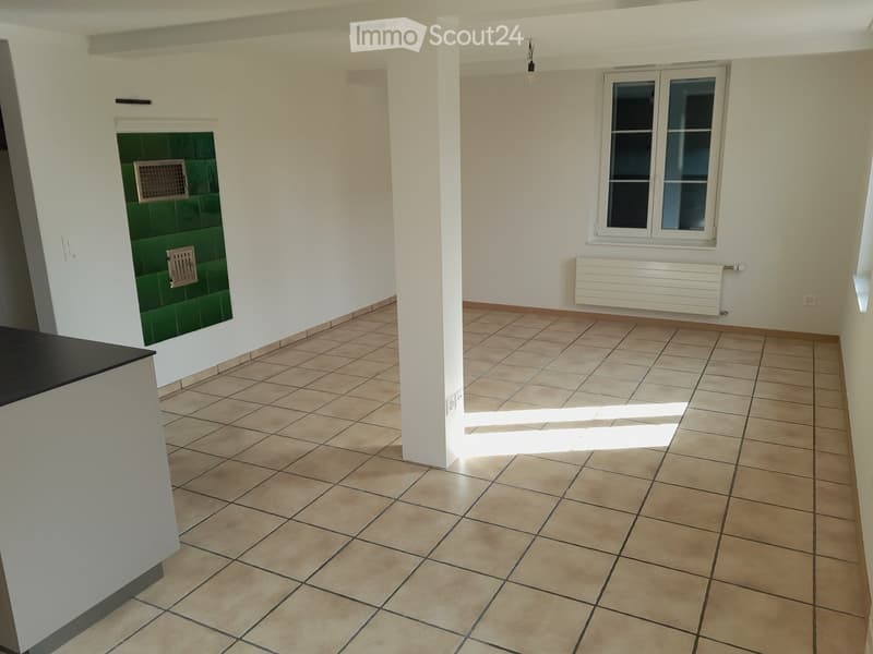 Empty hallway with tiled floor, white walls, a window, and a radiator. Green tiled section visible on one wall.