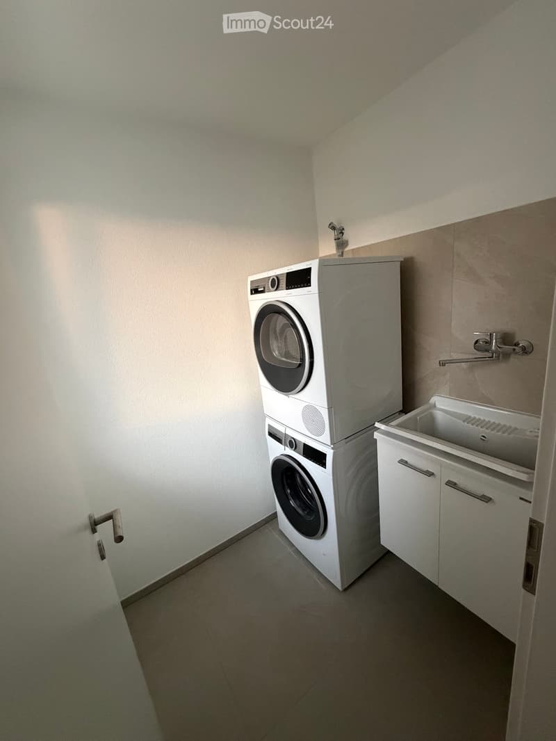 Modern bathroom with a stacked washing machine and dryer, a white sink with a faucet, and white cabinets.