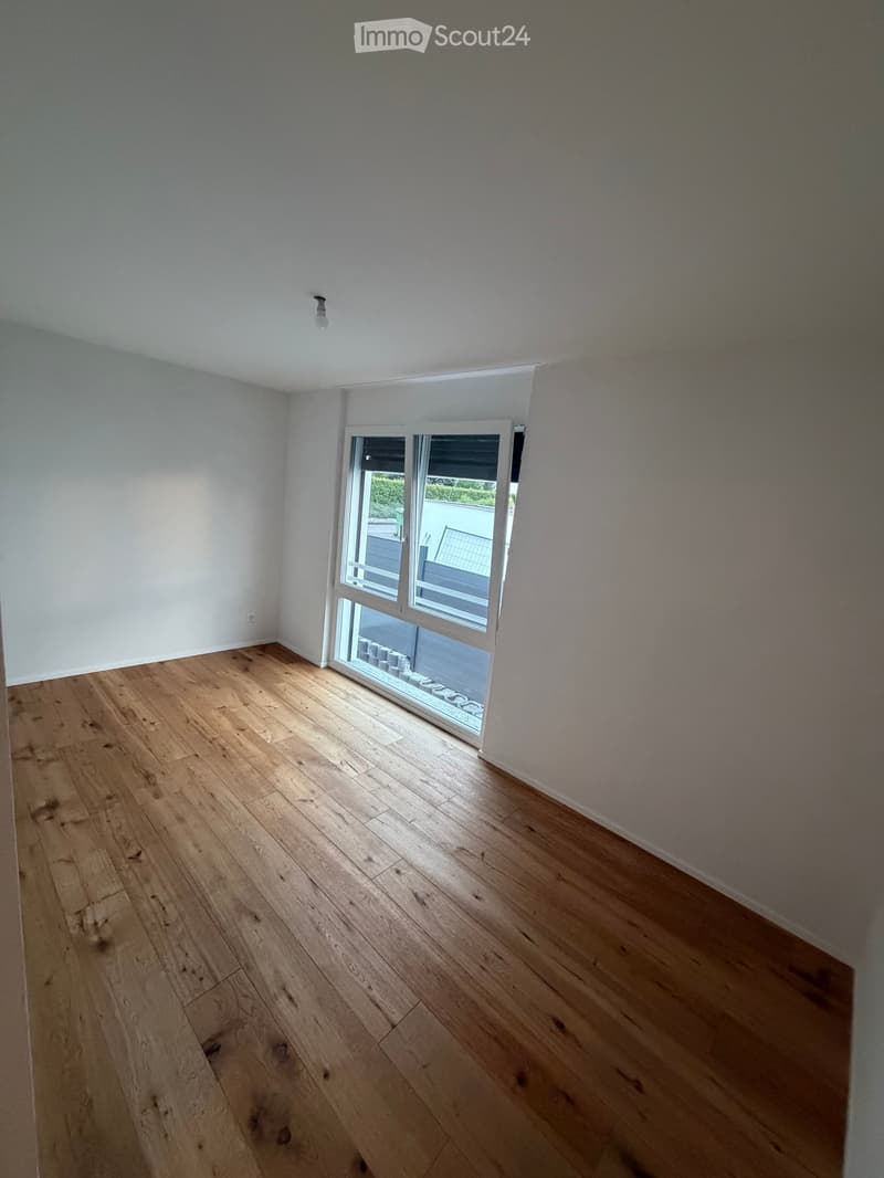 Empty room with wooden flooring and white walls, featuring a large glass door leading to an outdoor area.
