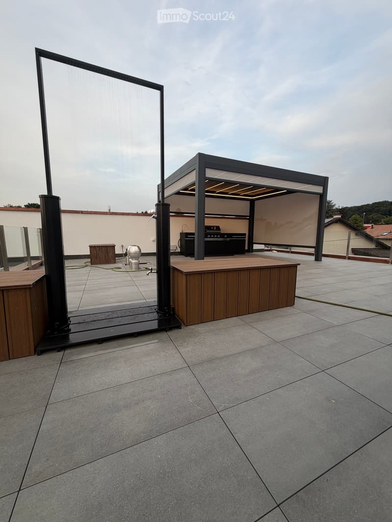 Roof terrace with tiled flooring, wooden decking, covered outdoor kitchen area, and a large retractable screen.