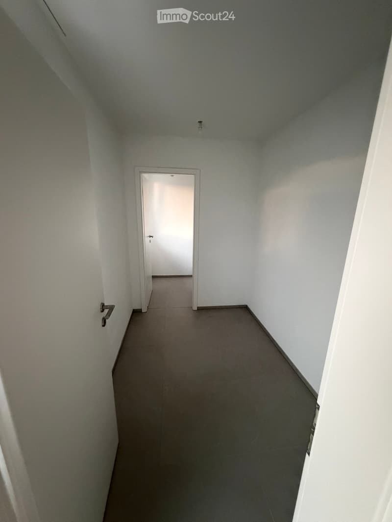 Empty hallway with white walls, gray tiled floor, and a single door at the end.