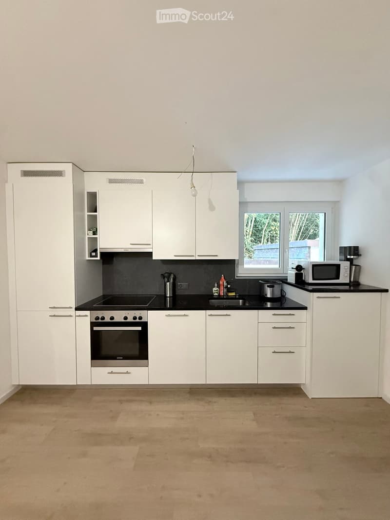 Modern kitchen with white cabinets, black countertops, and stainless steel appliances including an oven, microwave, and sink.