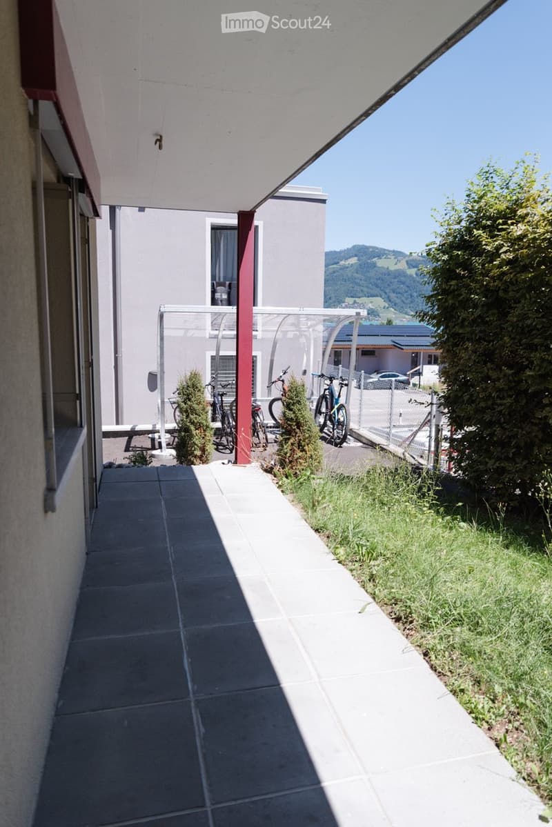 Balcony with tiled floor, covered roof, bicycles, and a view of the surrounding landscape and buildings.