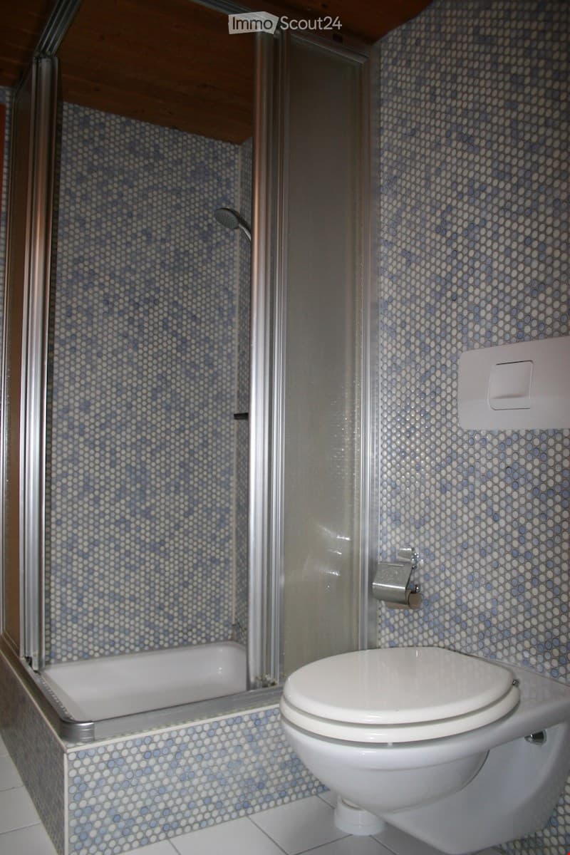 Bathroom with a toilet, bathtub, and shower area. The walls and floor are tiled in a blue and white pattern.