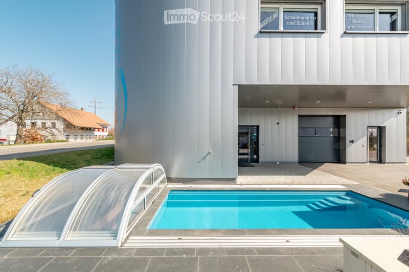 Modern building with a swimming pool and a covered patio area. The building has a sleek, contemporary design with large windows and signage.