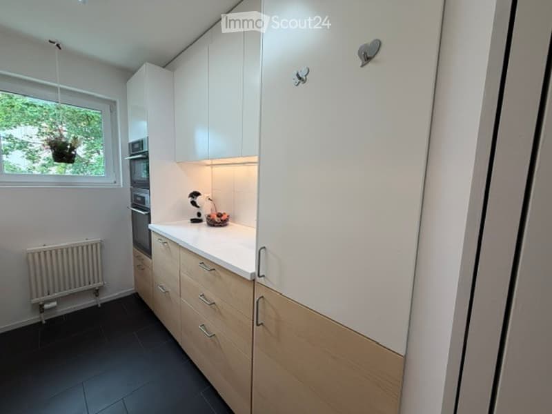 Modern kitchen with white cabinets, wooden drawers, built-in oven, and a fruit bowl on the counter.