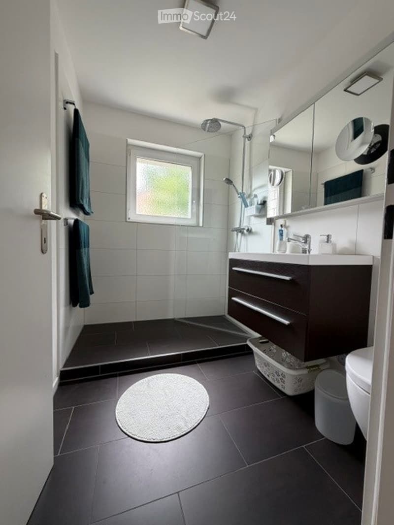 Modern bathroom with dark tiles, a large mirror, a sink with a cabinet, a shower, and towels.