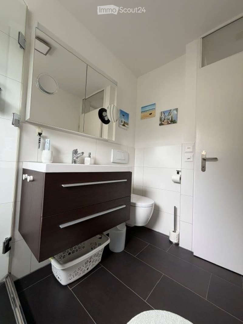 Modern bathroom with dark brown cabinet, white sink, mirror, toilet, and small decorative photos on the wall.