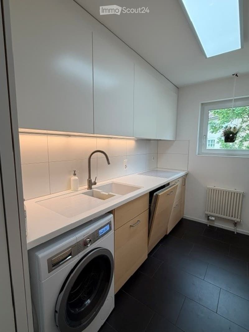Modern kitchen with white cabinets, a double sink, a washing machine, and a window with a plant visible outside.