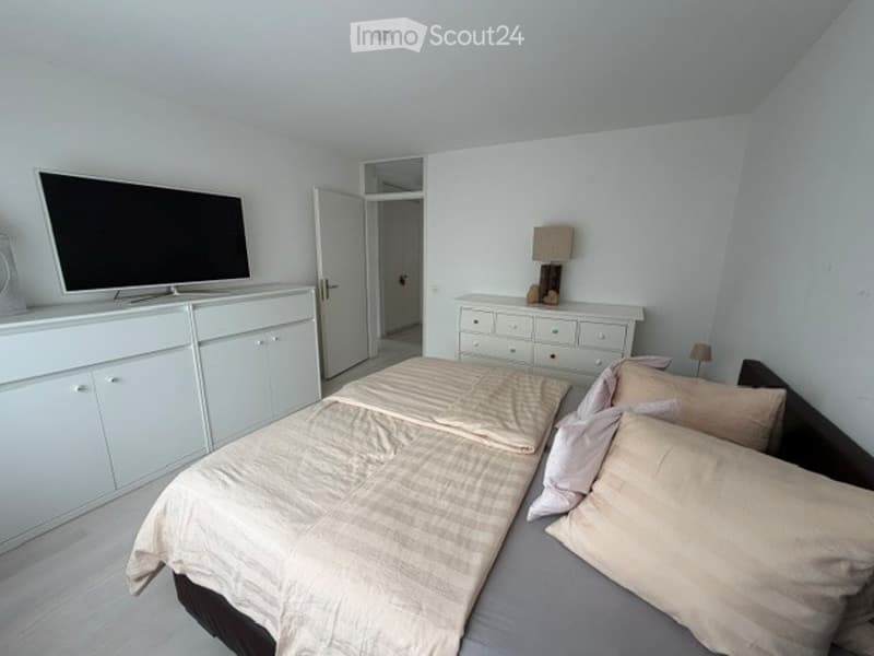 Bright bedroom with a double bed, nightstand with lamp, dresser, and television on a cabinet.