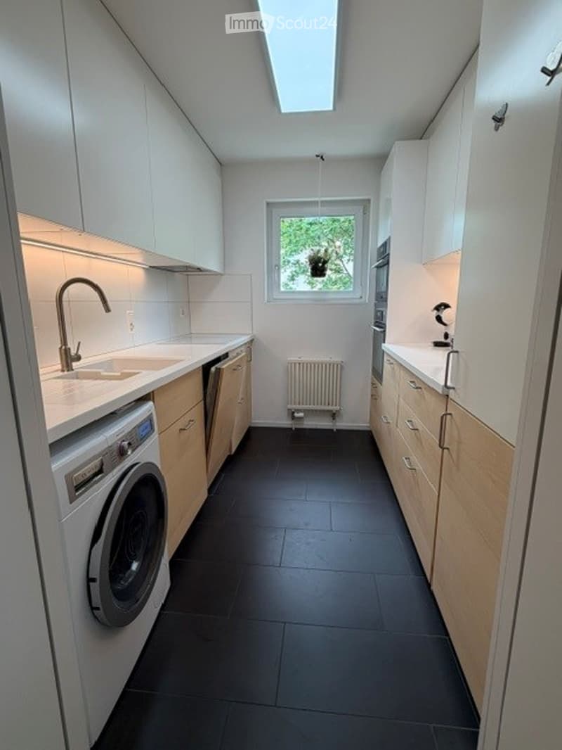 Modern kitchen with white cabinets, black tiled floor, sink, faucet, oven, washing machine, and radiator.