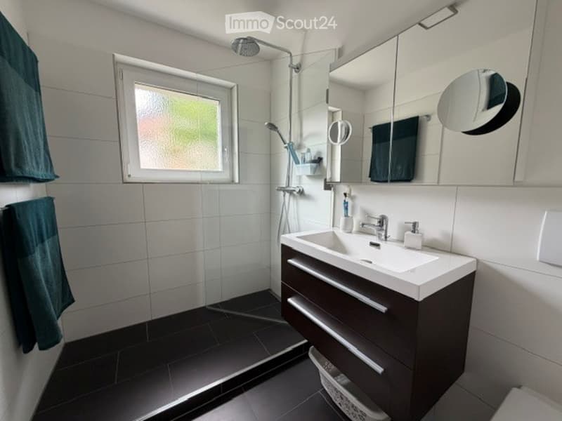 Modern bathroom with white tiles, dark wooden cabinet, large mirror, and shower area.