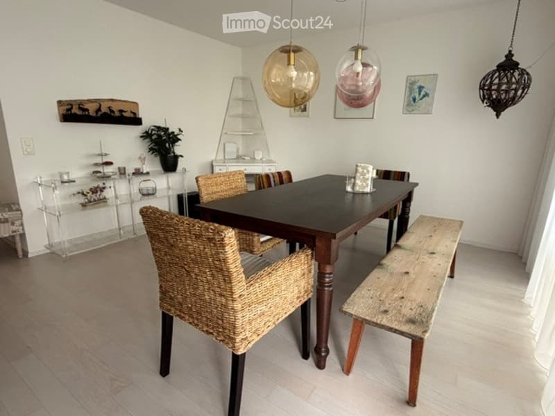 Dining room with a dark wooden dining table, wicker chairs, a wooden bench, pendant lights, and a potted plant on a shelf.
