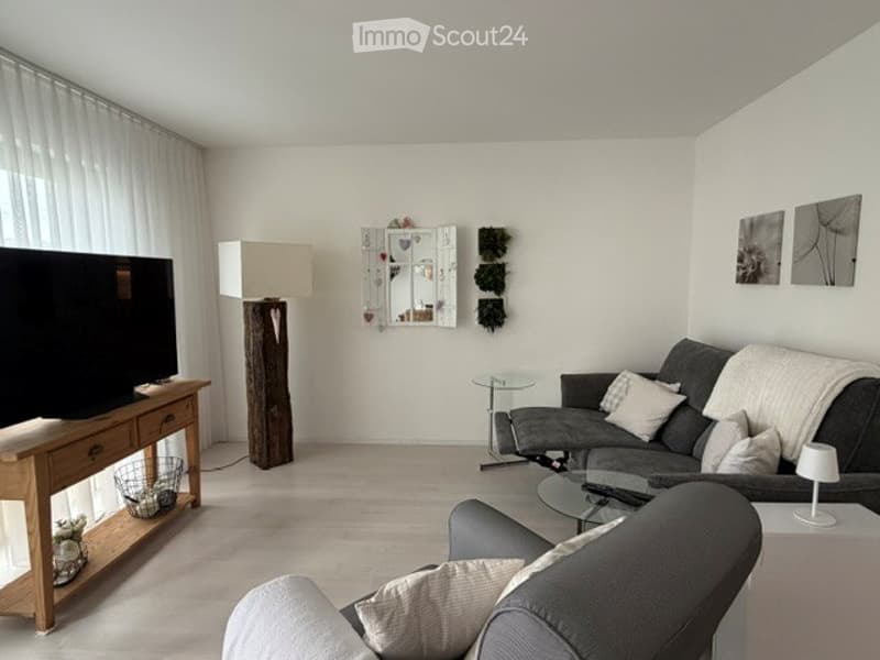 Modern living room with white walls, light wood flooring, grey sofa, coffee table, floor lamp, and decorative wall art.