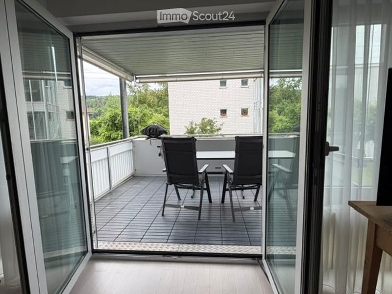 Balcony with tiled floor, glass railings, and outdoor furniture including chairs and a table.
