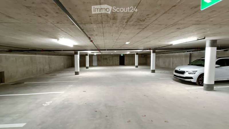 Underground parking area with concrete pillars, a parked white car, and fluorescent lighting.