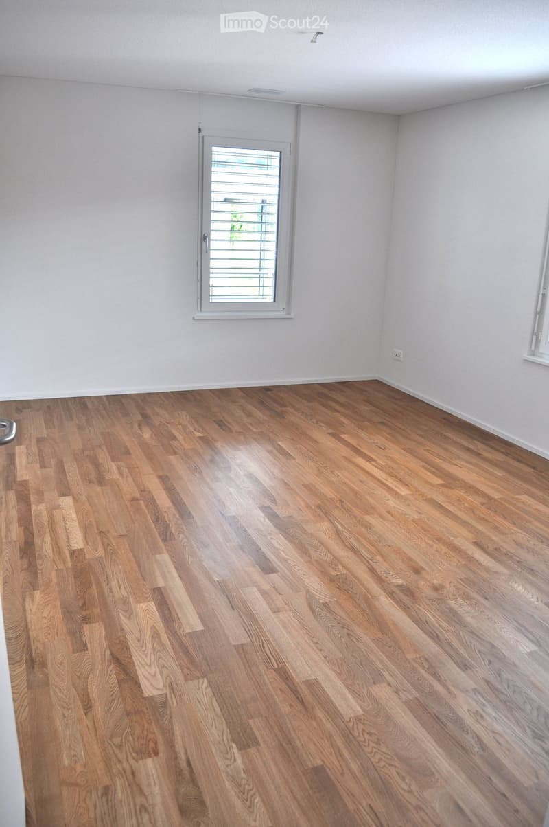 Empty room with wooden flooring and white walls, featuring a window with blinds and a door.