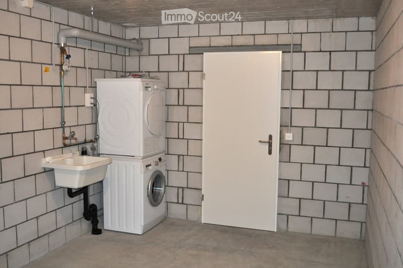 Utility room with white tiled walls, a stacked washer and dryer, a small sink, and a door.