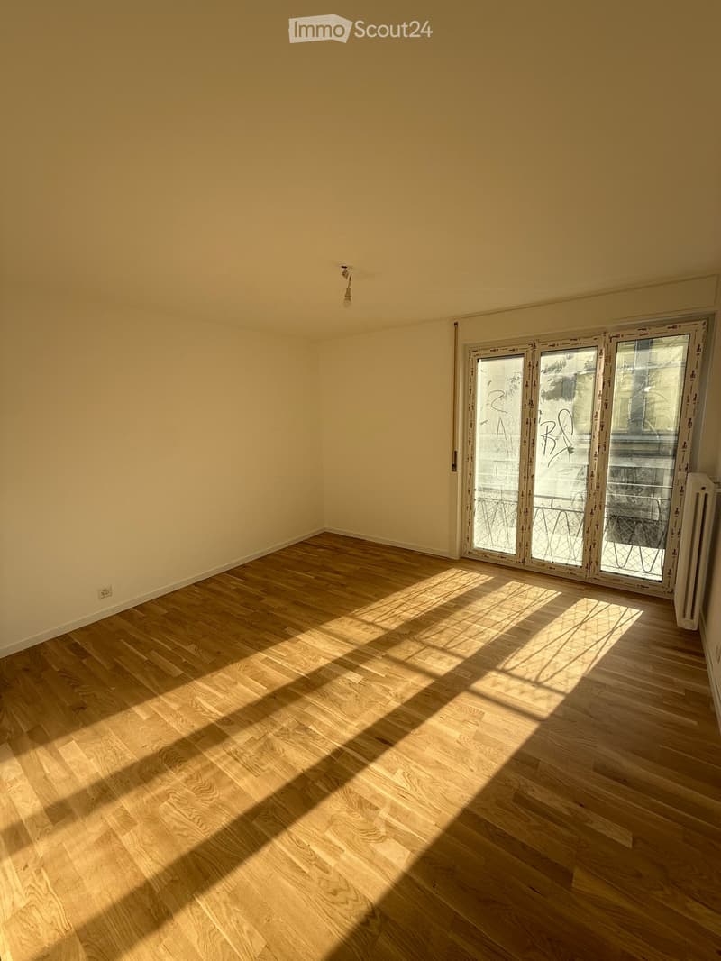 Empty room with light wooden flooring and cream-colored walls, featuring a large sliding glass door leading outside.