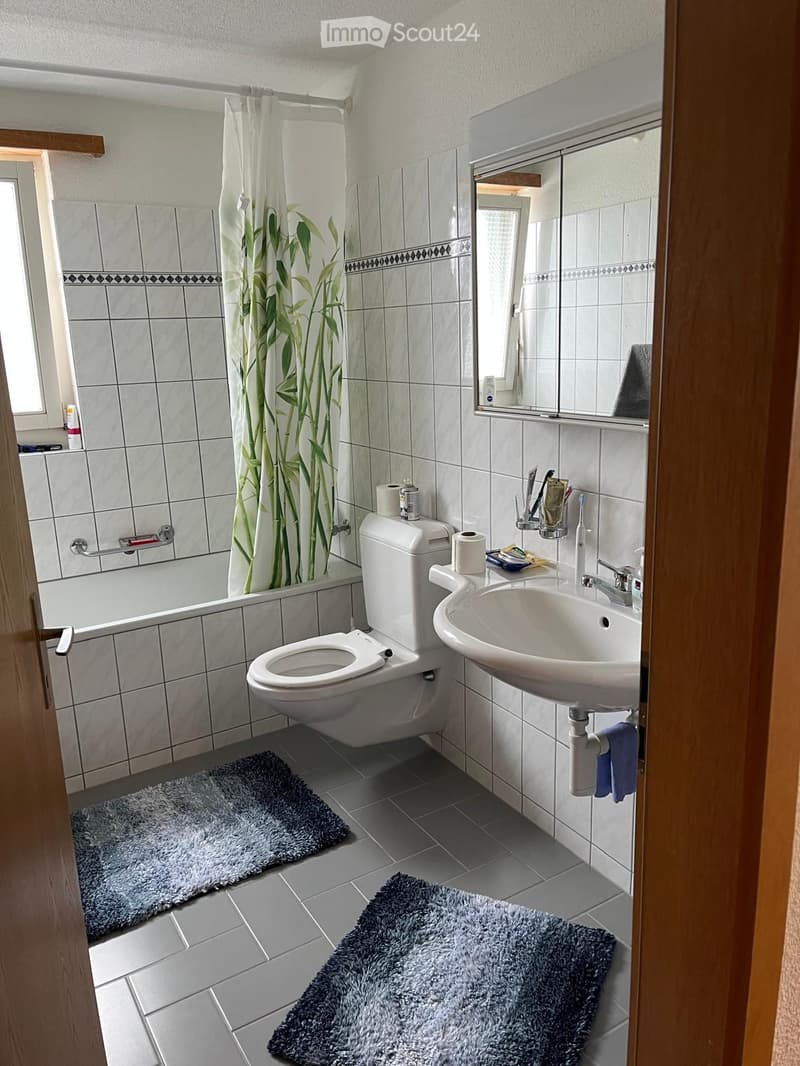 Bathroom with bathtub, toilet, sink, mirror, blue towels, white tiles, and shower curtain