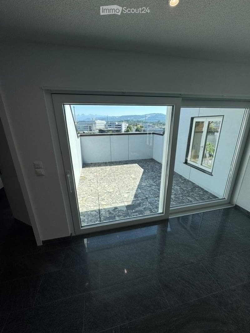Empty room with dark tiled floor, large sliding glass door leading to a balcony with a view of mountains and cityscape.