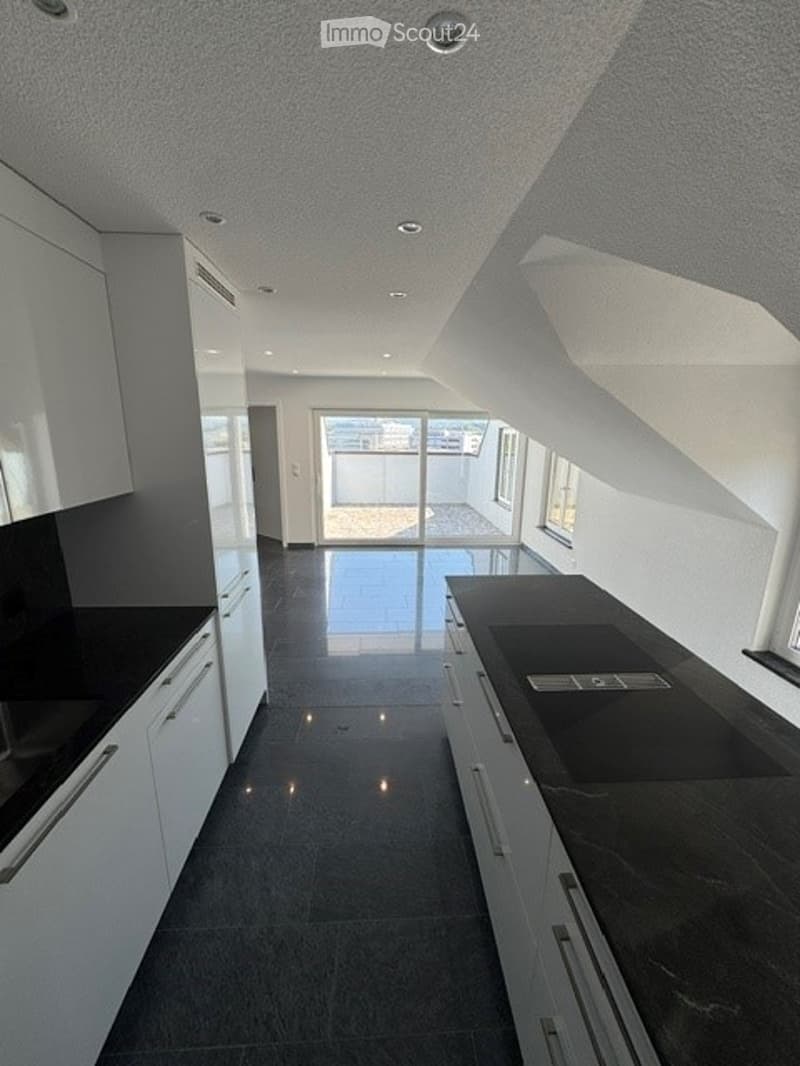 Modern kitchen with white cabinets, black countertops, and a sleek design. Features include a large window and a sliding glass door leading to a balcony.