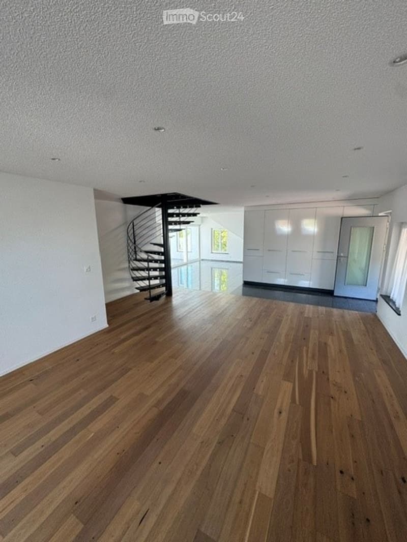 Empty room with wooden flooring, white walls, and a modern staircase leading to an upper level. No furniture or equipment is present.