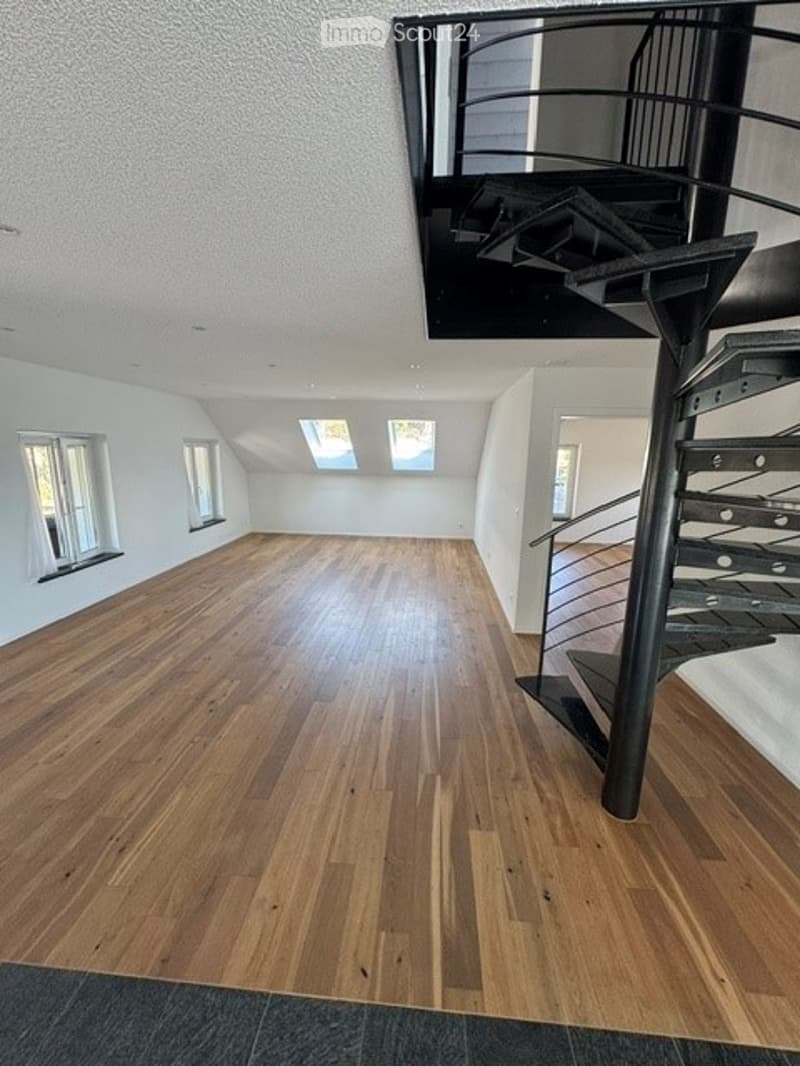 Completely empty room with wooden flooring, white walls, and a modern spiral staircase leading to an upper level. Skylights and windows provide natural light.