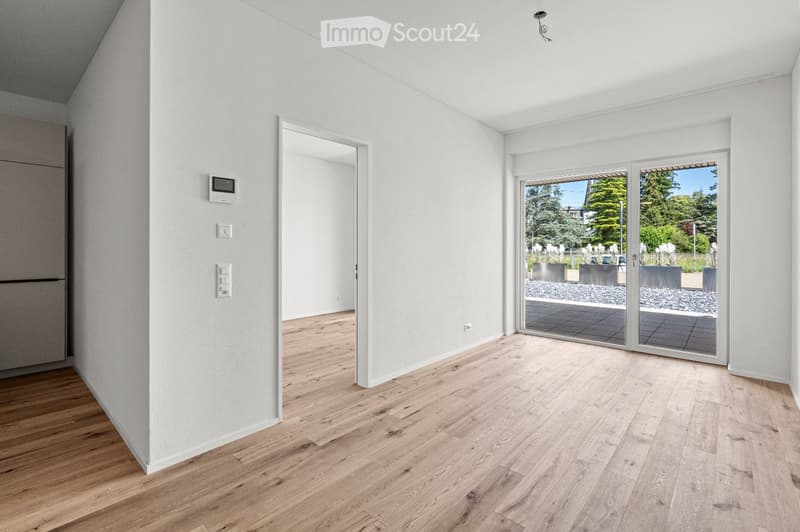 Empty room with light wooden flooring, white walls, and large sliding glass doors leading to an outdoor area.