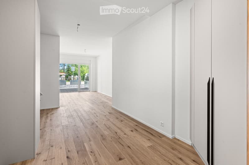 Empty hallway with light wooden flooring and white walls, featuring a large glass door leading to an outdoor area.