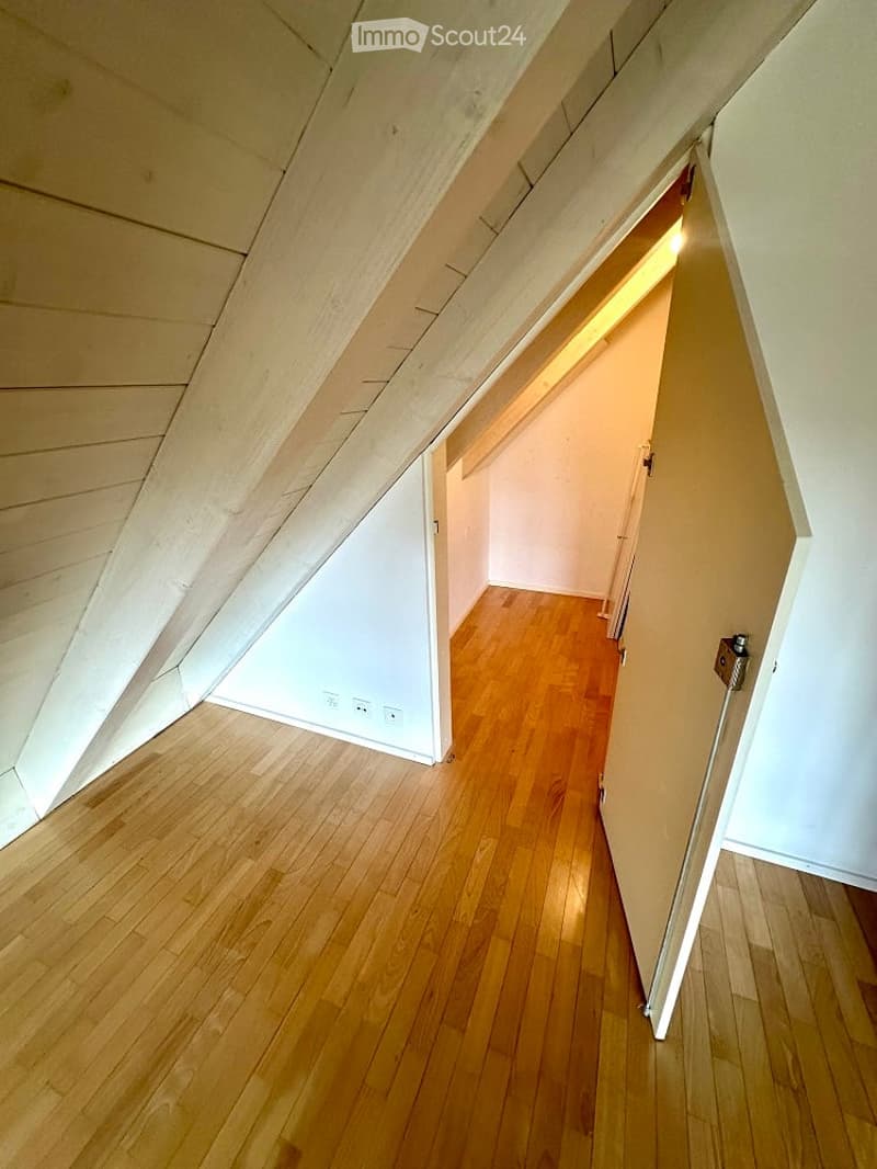 Attic room with wooden floor and ceiling, sloping ceiling, an open door.