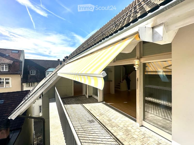 A covered balcony on a building with a brick wall, yellow and white awning, and glass door.