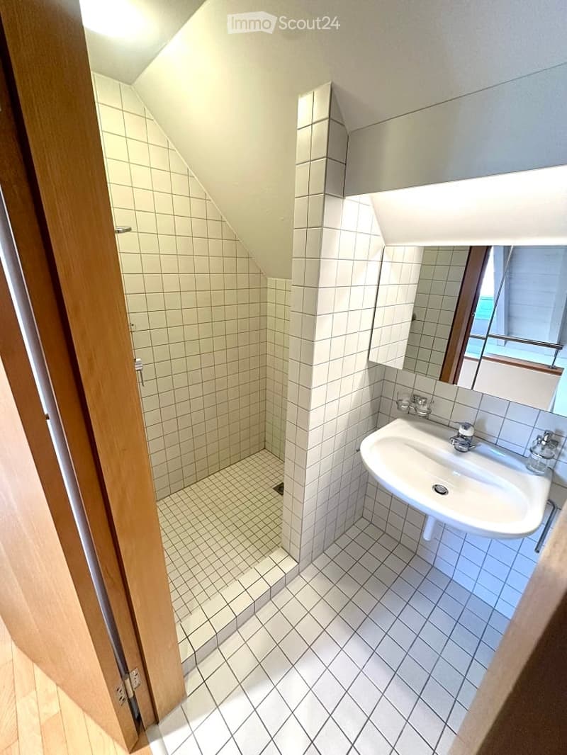 A white tiled bathroom with a walk-in shower, a sink, a mirror, and a small toilet window