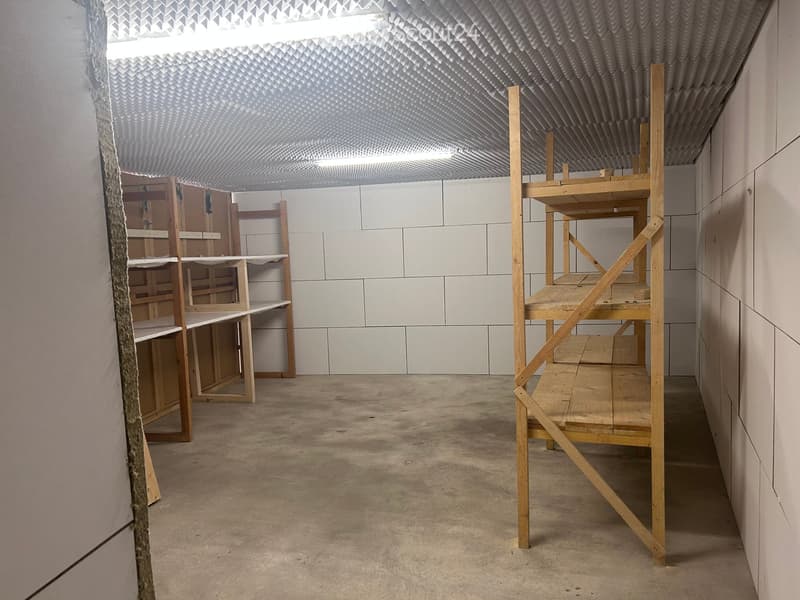 Empty room with unfinished concrete floor, white tiled walls, and wooden shelving units.