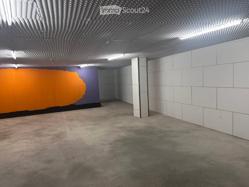 Empty room with white tiled walls, a textured ceiling, and a concrete floor. A colorful mural is visible on one wall.