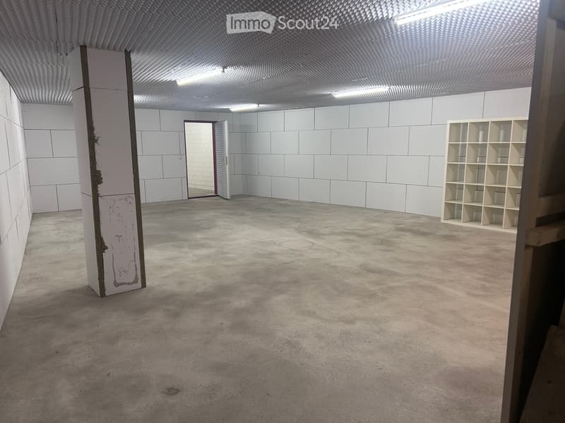 Empty room with white tiled walls, concrete floor, and a single wooden shelving unit in the corner.
