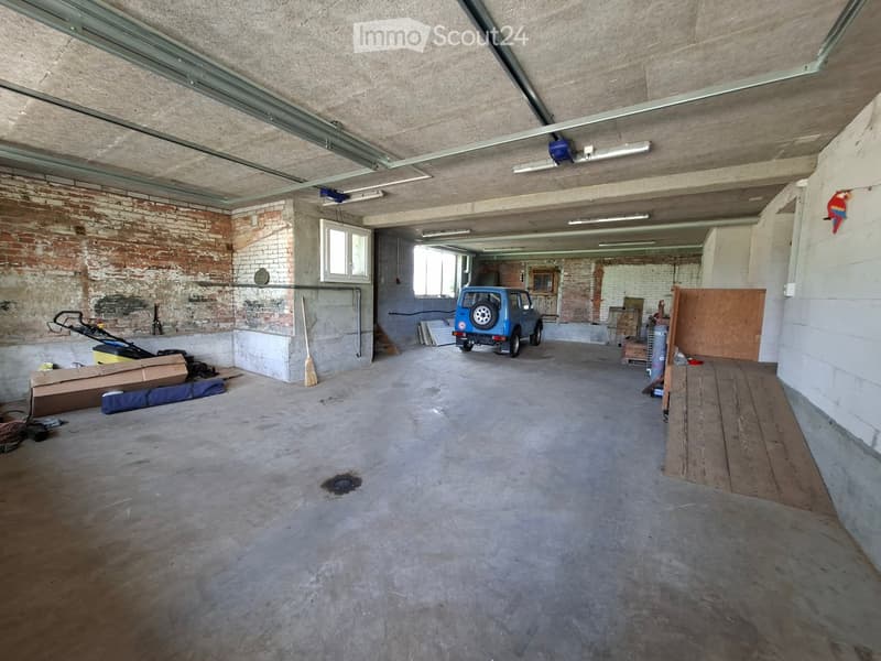 Empty garage with exposed brick walls, concrete floor, and a parked vehicle. No furniture or equipment.