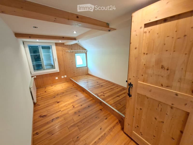 Empty room with wooden flooring, white walls, and exposed wooden beams on the ceiling. Features a window with shutters and an open wooden door leading to another space.