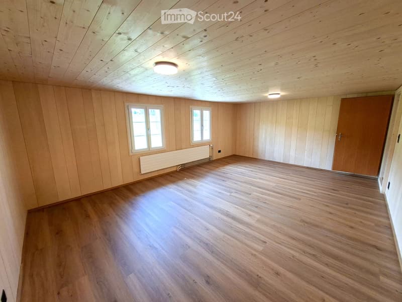 Empty room with wooden walls, wooden floor, and two windows. No furniture or equipment present.