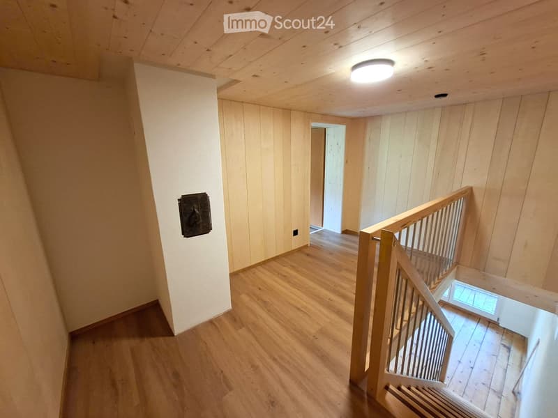 Wooden staircase with a handrail, light wooden walls, and a ceiling light fixture. The hallway has wooden flooring and a small window at the top of the stairs.