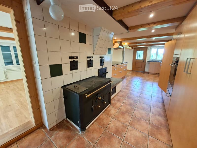 Kitchen with tiled walls, wooden beams, stove, cabinets, sink, and tiled floor.