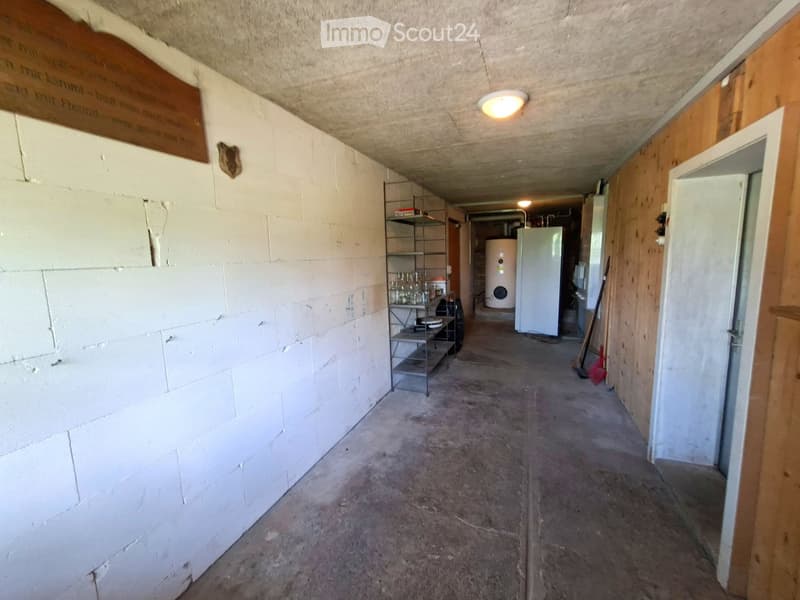 Empty hallway with concrete walls, wooden paneling on one side, metal shelving unit, and a water tank in the background.